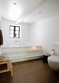 Modern bathroom with brown floor tiles and steps leading to built-in bathtub below window
