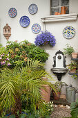 Area in courtyard decorated with wall-mounted plates, antique, ornate wall-mounted sink and potted plants