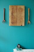 Artistic still-life arrangement of wooden forks and old chopping board on turquoise wall above tiny Flamenco doll sitting on radiator