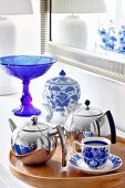 Chrome teapots and blue and white crockery on wooden tray in front of blue glass goblet