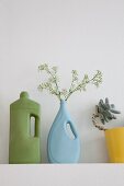Industrial plastic bottles painted blue and green on shelf, one holding sprig of flowers