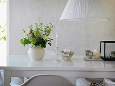 Romantische Tischdekoration mit Kerzenlicht und Blumenstrauß auf glänzender weißer Tischplatte