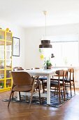 Retro chairs at white dining table below pendant lamp next to display case with yellow frame