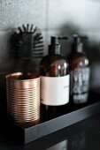 Copper-coloured metal beaker and soap dispenser on black shelf