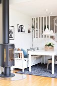 White table and bench under two pendant lamps next to black, cast iron log burner
