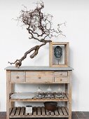 Gnarled branch and head of Buddha in wooden frame on top of simple wooden sideboard with drawers and shelves