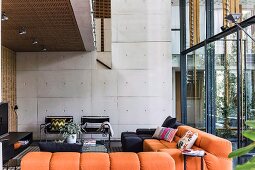 Modern lounge with orange upholstered sofa under gallery, in the background exposed concrete wall in contemporary architecture