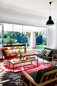 Gemütlicher Loungebereich mit 50er Jahre Polstermöbeln und farbenfrohem modernem Teppich, freier Gartenblick