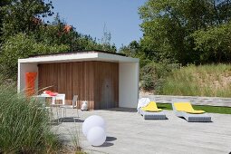 Terrassenplatz mit Sonnenliegen auf Holzboden vor modernem Poolhaus mit Aussendusche