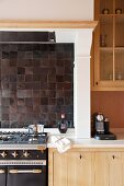 Gas cooker integrated into kitchen counter below dark tiled splashback and extractor in mantel hood