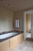 Fitted bathtub with marble surround and carved wooden front in renovated bathroom