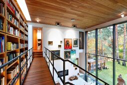 Bookcase on airy steel and wood gallery opposite glass wall with gallery of paintings on end wall