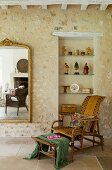 Wicker chair and footstool in front of glass shelves in niche in stone wall next to gilt-framed mirror