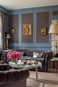 Button-tufted sofa below gilt-framed pictures on elegant wood panelling painted grey and blue
