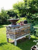 Barbecue and potted plants on counter made from reclaimed boards in sunny garden
