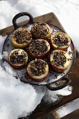 Halved apples filled with bird food in pan in snow