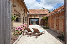 Sun loungers and pink hydrangeas in paved courtyard of renovated farmhouse