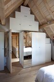 White, custom, fitted wardrobe with mirrored door in attic bedroom of modernised farmhouse