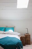 Zwei rustikale Holzblöcke als Nachttische neben Bett und weiß gestrichene Dachschräge mit Dachflächenfenster