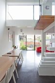 Zwei Holztische mit weissen Stühlen in modernem, offenem Wohnraum mit Galerie