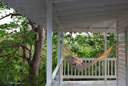 Hammock in evening sun on wooden veranda encircling beach house surrounded by trees & foliage plants