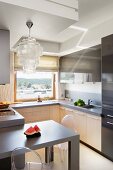 Elegant capiz shell pendant lamp above dining table in small fitted kitchen in shades of beige and grey