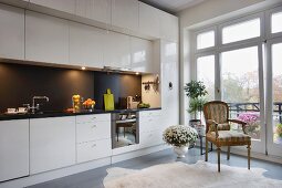 Eclectic interior with black and white, glossy kitchen counter and splashback, antique armchair and modern glass wall