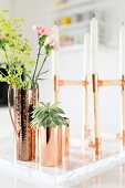 White candles in candelabra next to succulent and flowers in copper vases