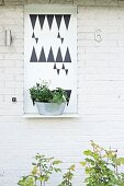 Planter on metal shelf with graphic pattern on whitewashed brick façade