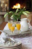 Tray of orange juice in front of vase of lilies on dining table