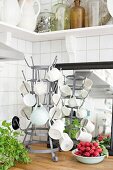 Cups hung on metal bottle rack and bowl of fresh radishes on wooden worksurface in corner of kitchen