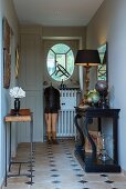 Table lamp on antique black console table and nostalgic tailors' dummy in traditional country-house hallway