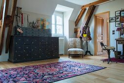 Rug on wooden floor in front of vintage chest of drawers next to window and armchair in corner