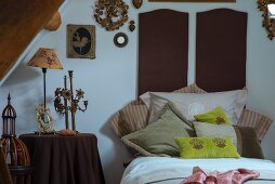 Vintage-style candelabra and table lamp on side table next to bed with scatter cushions arranged against dark brown bed headboards
