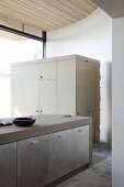 Concrete kitchen counter with built-in cupboards in front of multifunctional cupboard with wooden surfaces stained pale grey