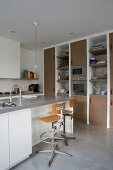 Kücheninsel, drehbare Retro Barhocker, oberhalb minimalistische Pendelleuchte mit Glühbirne in moderner, offener Küche