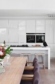 Detail of dining area in open-plan kitchen with gas hob on minimalist counter, fitted appliances and fitted cupboards with glossy white fronts