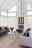 Sofa and armchairs in various shades of grey around retro coffee table in high-ceilinged interior