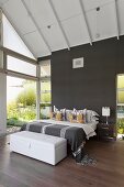 Double bed and white trunk in modern bedroom with wall painted dark grey
