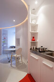 Blick von Miniküche in kreisförmigem Wohnbereich, mit abgehängtem Deckenfeld über Tisch und Ghost Stuhl