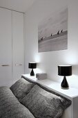 Grey patterned bed linen on bed, black table lamps on shelf and black and white photo of sailing boats