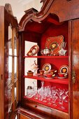Antique, Art Nouveau crockery and glasses on red shelves in open. Baroque-style display cabinet