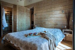 Frühstückstablett auf Doppelbett mit Tagesdecke, in rustikalem Schlafzimmer mit horizontaler Holzverschalung