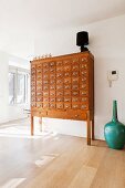 Vintage wooden apothecary cabinet and turquoise floor vase on wooden floor in minimalist interior