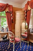 Corner of bedroom - chair with carved backrest painted antique white in front of cheval mirror on blue carpet with pattern of stars
