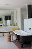 Free-standing bathtub with black, glossy outer wall next to turned wooden stool in modern bathroom
