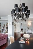 Chandelier with small black lampshades and glass pendants above dining table in open-plan interior with walls painted pale grey