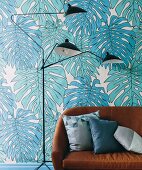 Brown leather sofa and classic floor lamp in front of wallpaper with turquoise philodendron motifs