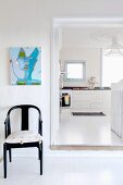 Schwarz lackierter Armlehnstuhl neben offener Tür und Blick in weiße Küche