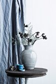 Dried flowers in a striped ceramic vase on a rustic bistro table in front of a curtain